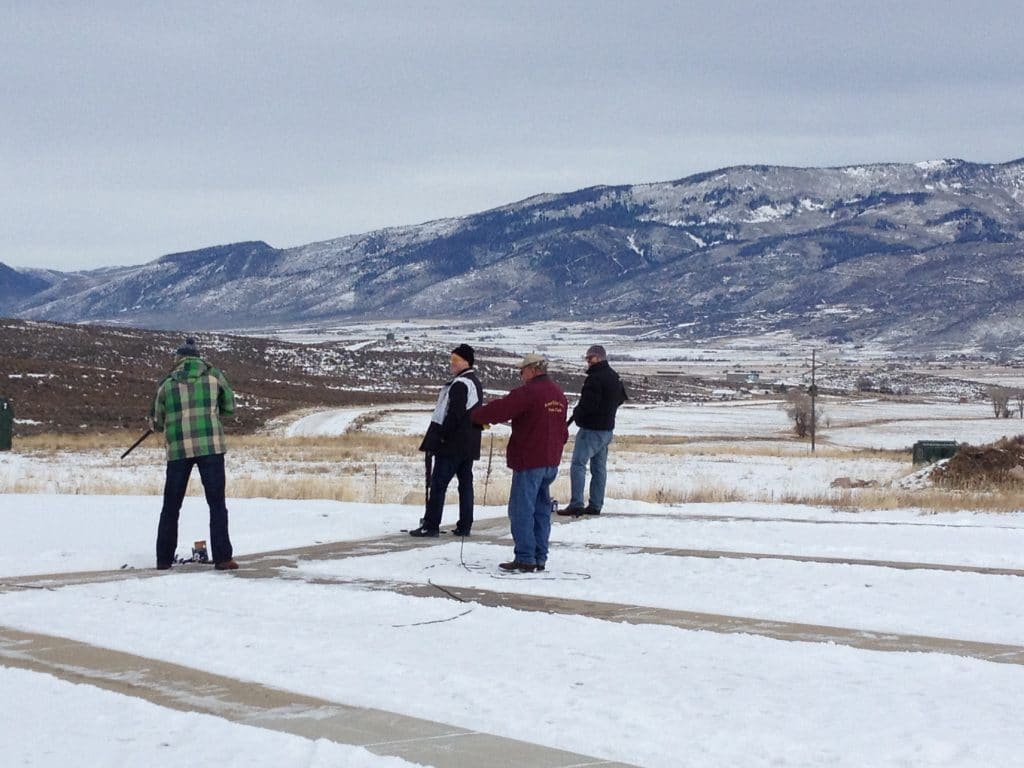 a group preparing to shoot 12-gauge shot guns at the shooting range with a layer of snow on the ground