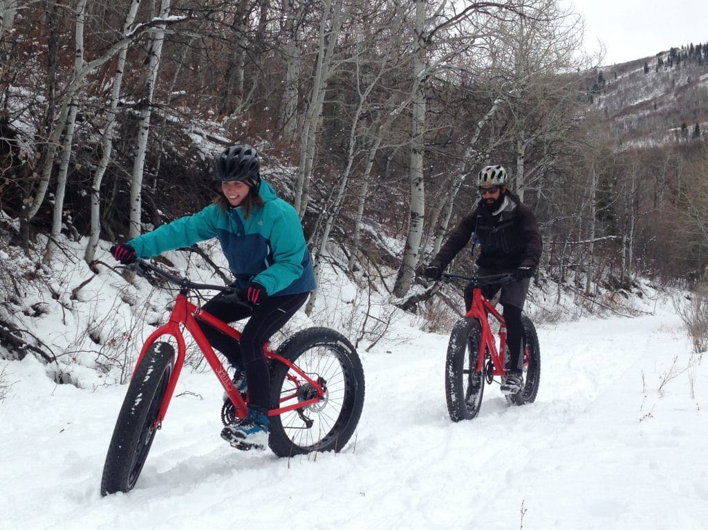 two people riding bikes with wide tires through snow-covered trails