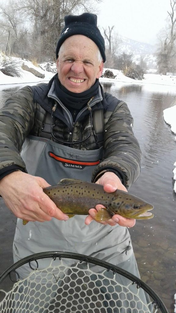 Man standing with brown trout in hand while it's snowing outside